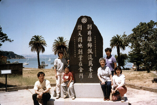 A photograph of Chinese Progressive Association members sitting around a Chinese monument at Angel Island Immigration Station in San Francisco