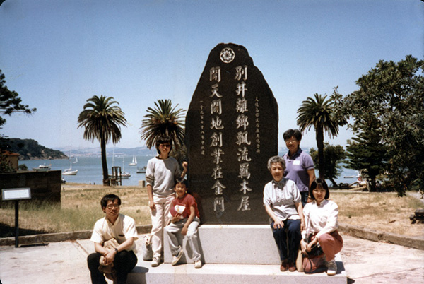 A photograph of Chinese Progressive Association members sitting around a Chinese monument at Angel Island Immigration Station in San Francisco