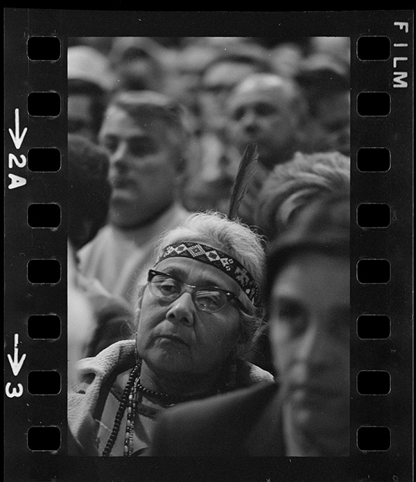 a black and white film photo of an indigenous woman in a crowd